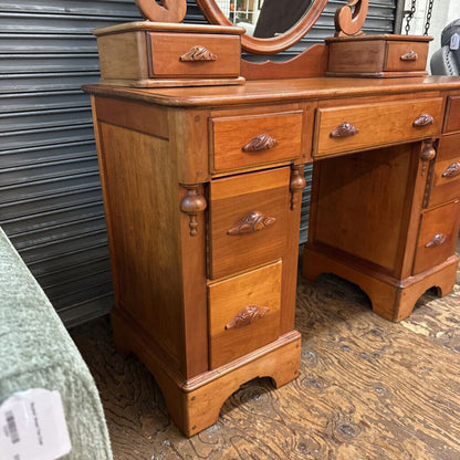 Wooden vanity with drawers and a mirror on top, against a metal shutter background.
