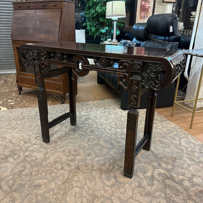 Dark wooden desk with intricate carvings in a room setting.