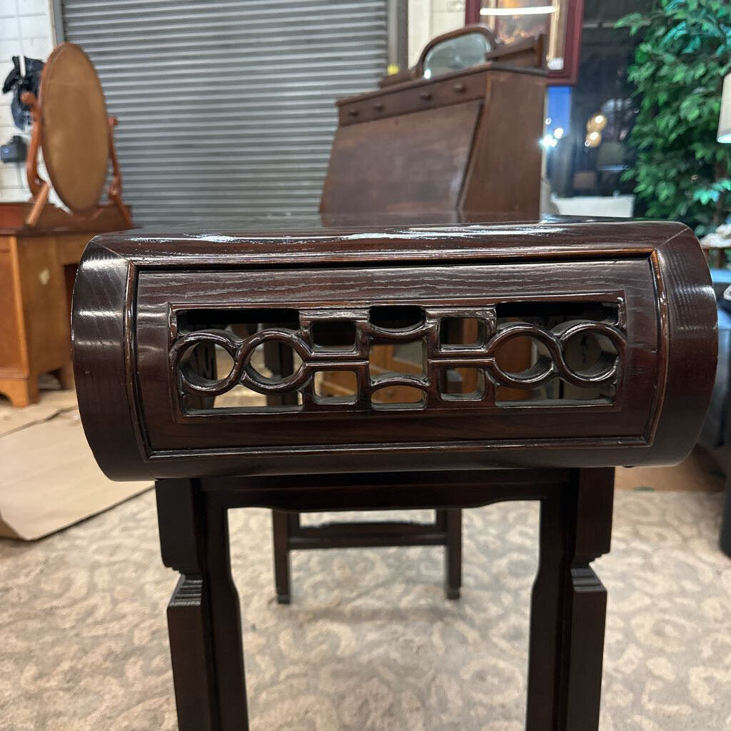 Dark wooden decorative item with intricate carvings on a stand, blurred background