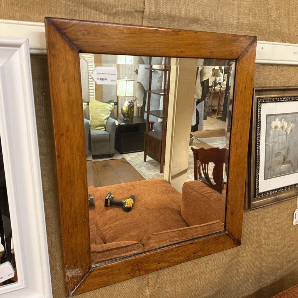 Wooden-framed mirror reflecting a room with furniture and decor.