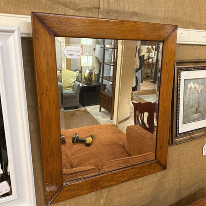 Wooden-framed mirror reflecting a room with furniture and decor.