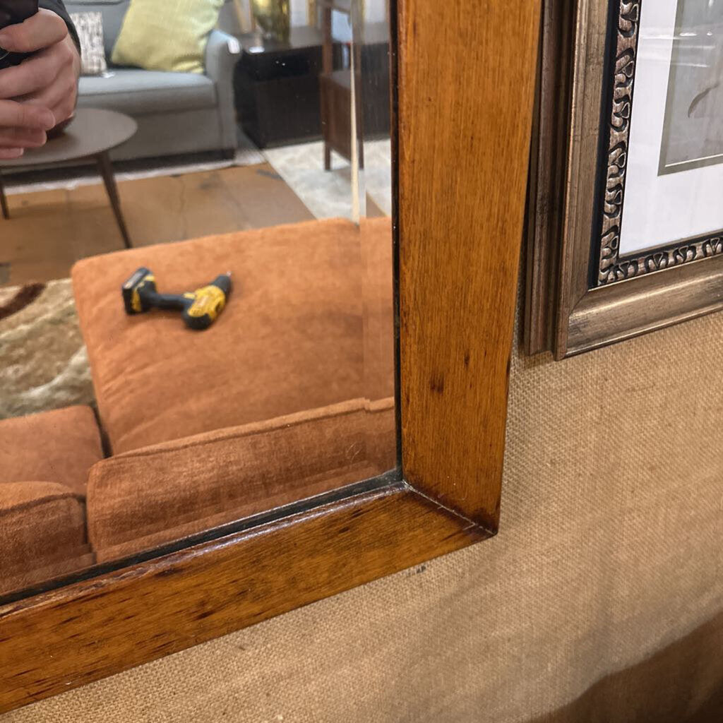 Close-up of a wooden-framed mirror with a tool on a brown surface.