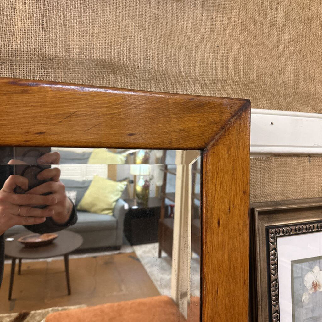 Wooden mirror frame with a blurred reflection of a living room.