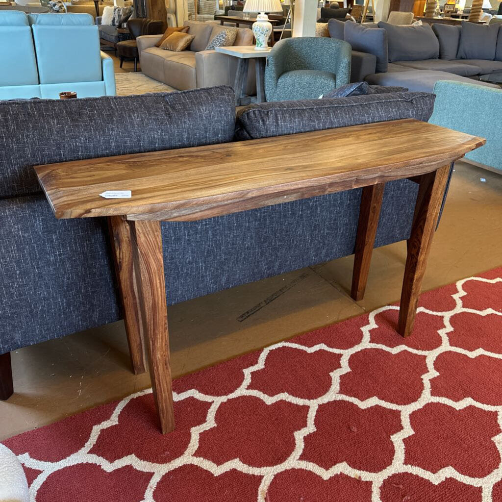 Wooden console table in a furniture store with blue sofas and a red patterned rug.