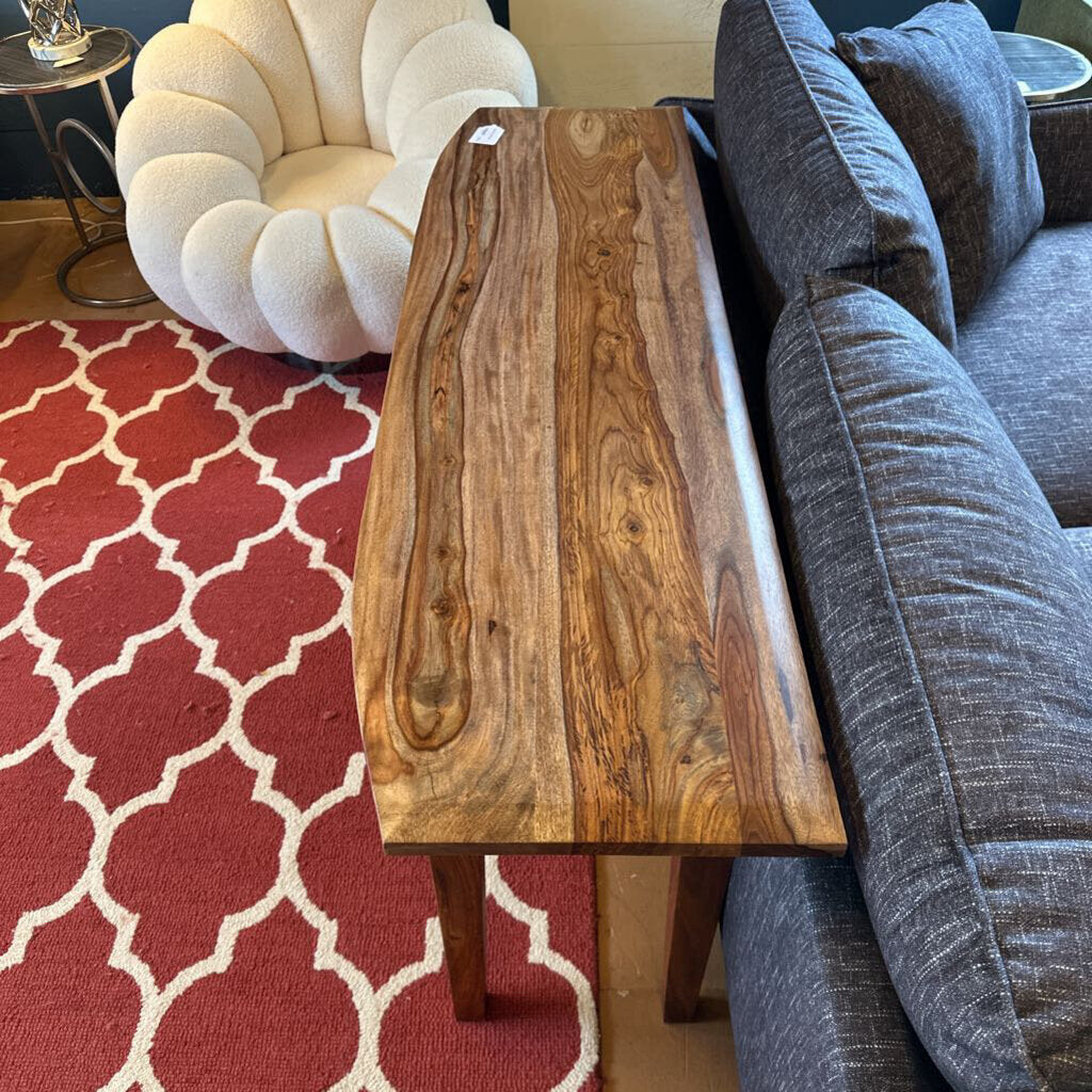 Wooden coffee table in a living room with a red patterned rug and gray sofa.