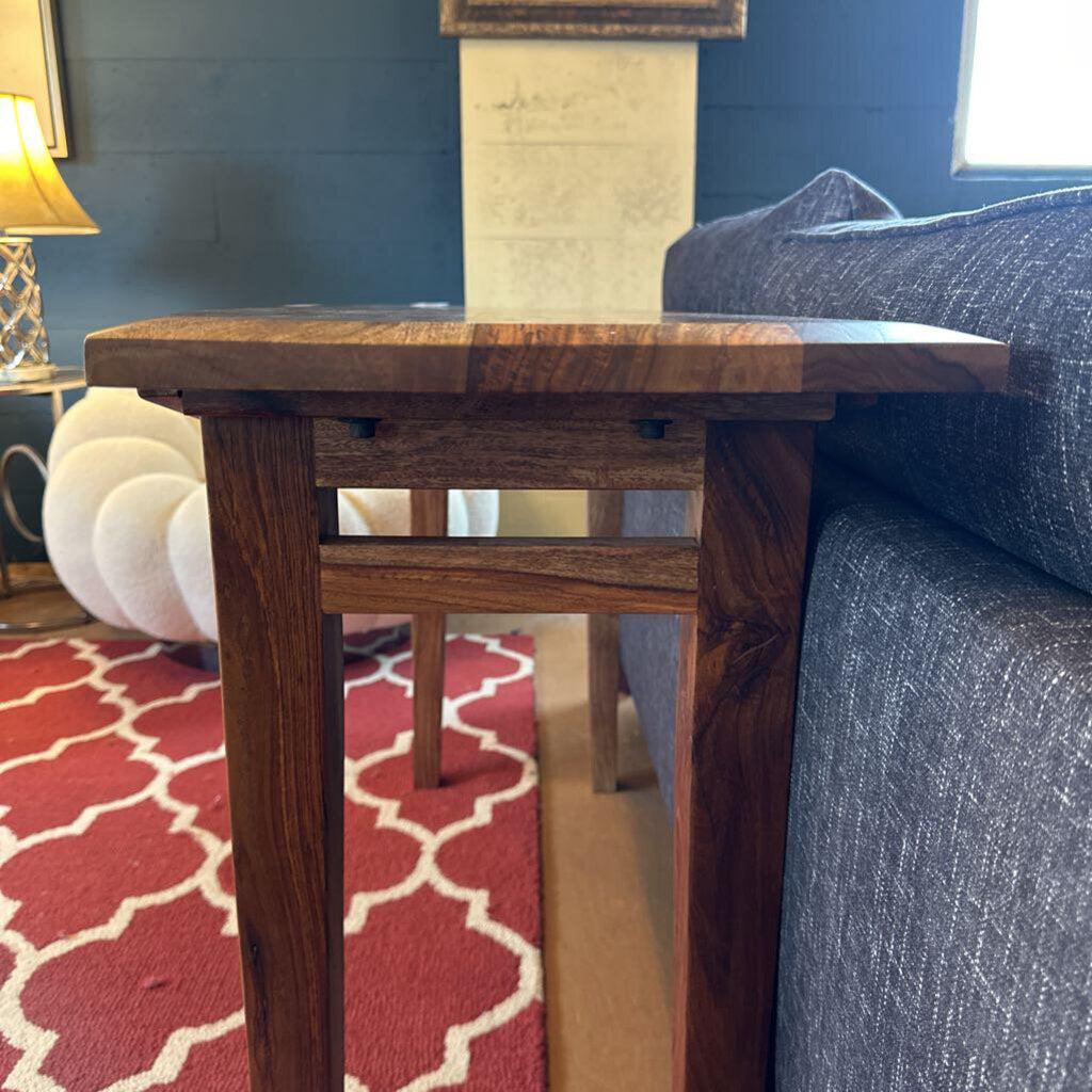 Wooden side table in a living room setting with a blue sofa and red patterned rug.