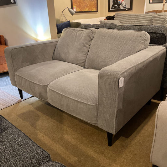 Gray sofa in a showroom setting with other furniture.