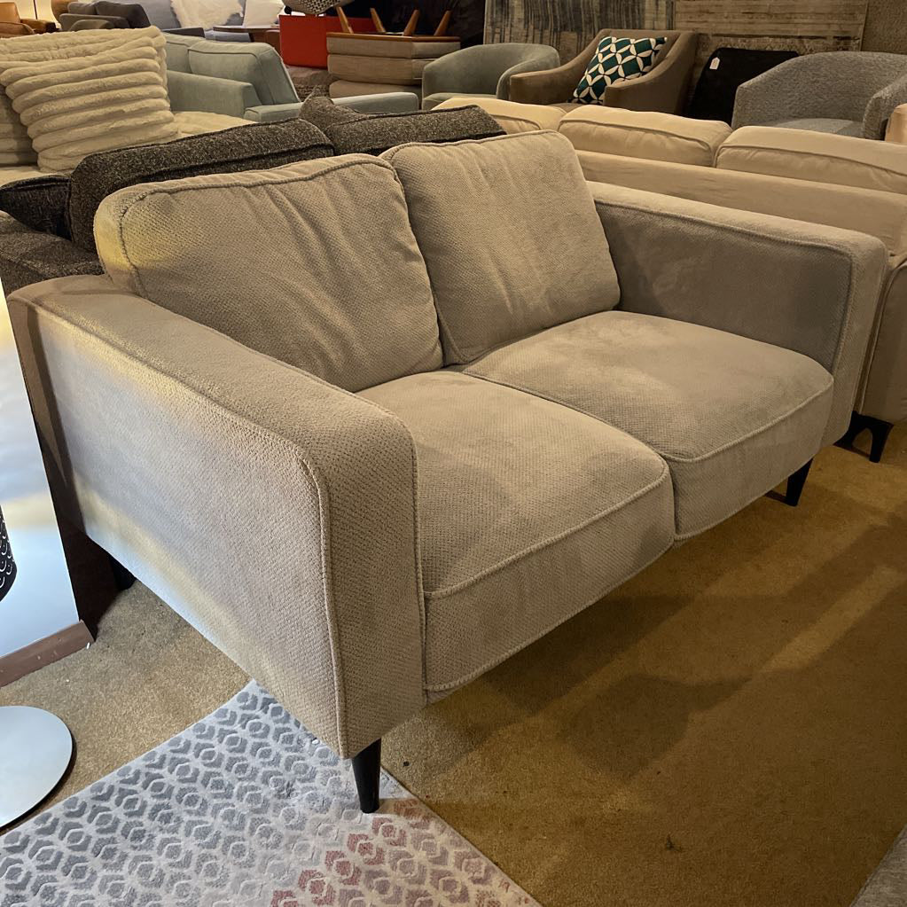 Beige sofa in a furniture store setting with other sofas and decor items.