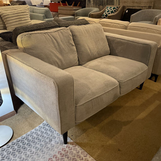 Beige sofa in a furniture store setting with other sofas and decor items.