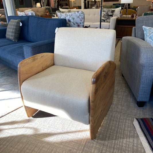 White armchair with wooden arms and legs in a showroom setting with other furniture.