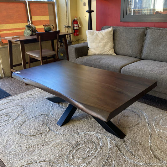 Wooden coffee table in a living room setting with a gray couch and dining area.