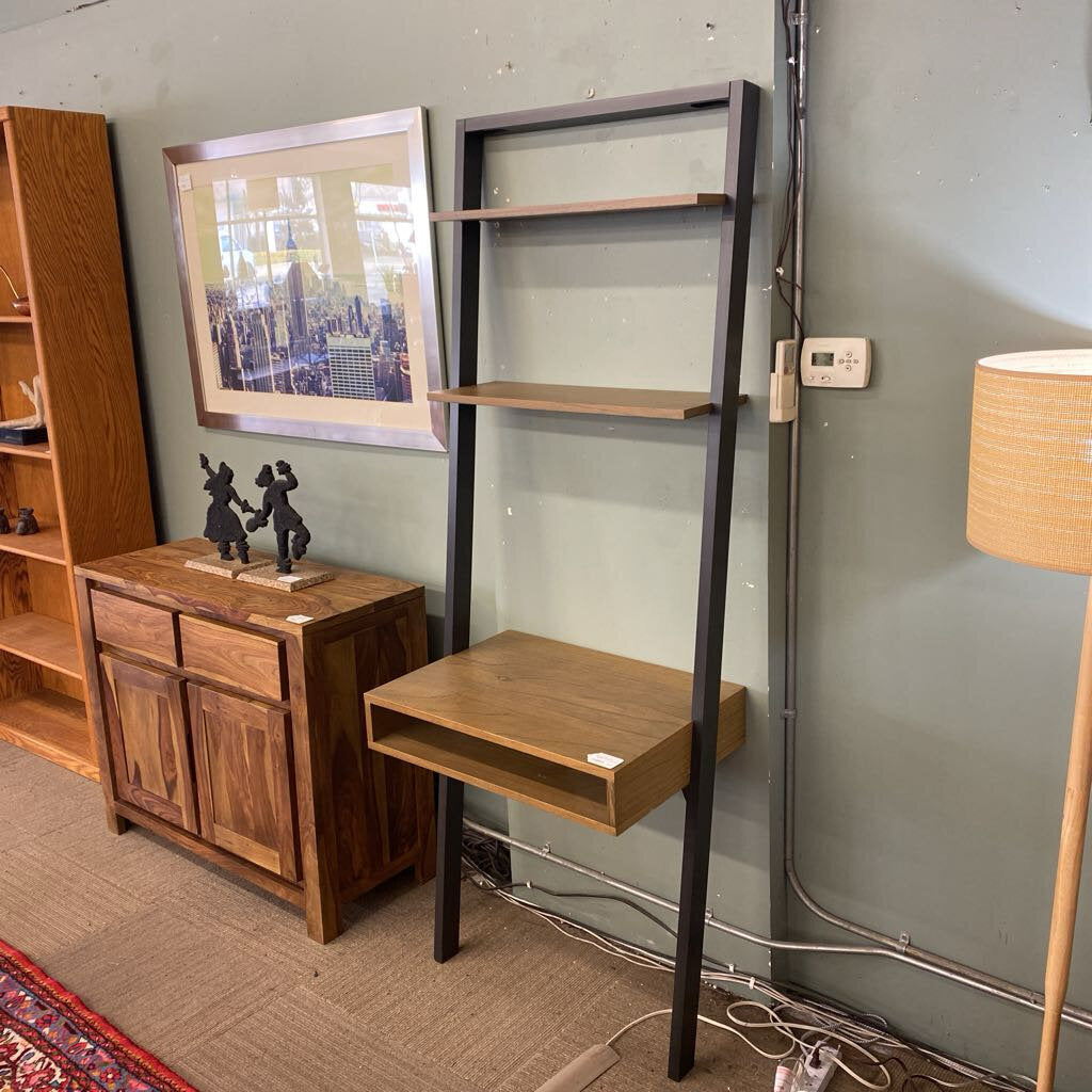 Wooden desk with shelves against a wall, next to a wooden cabinet and lamp.