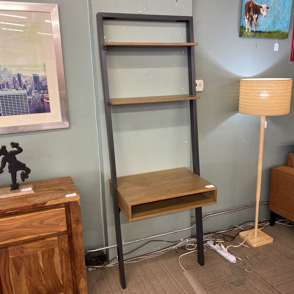 Wooden shelf unit with a desk against a wall with framed pictures.