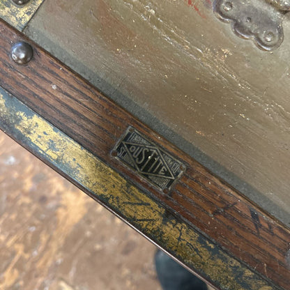 Close-up of an antique suitcase with a visible brand logo on a wooden surface.