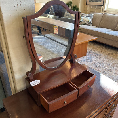 Wooden vanity mirror with a drawer on a wooden surface, with a living room in the background.