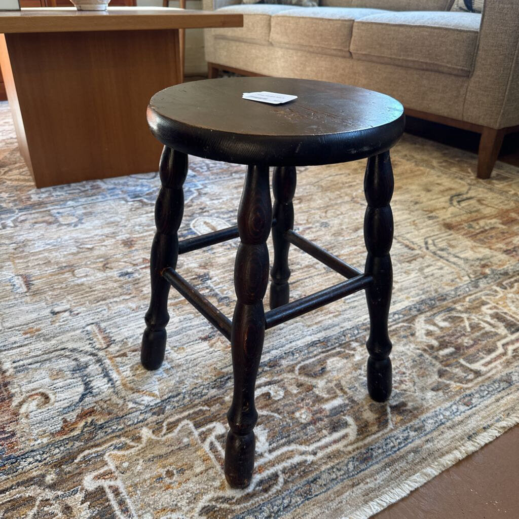 Wooden stool on a patterned rug with a couch and table in the background