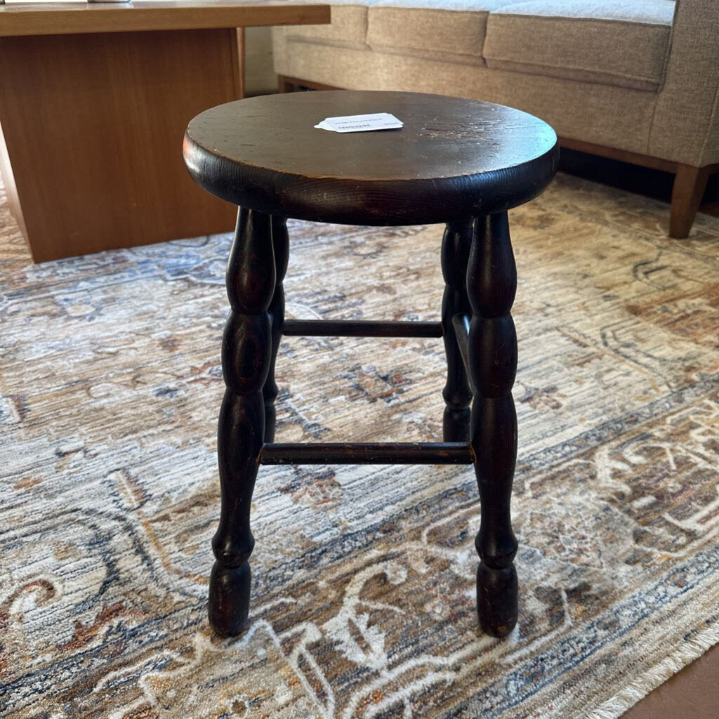 Wooden stool on a patterned rug with a blurred background