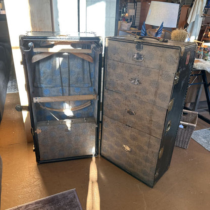 Vintage-style trunk with open lid revealing blue fabric inside, on a wooden floor.