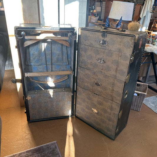 Vintage-style trunk with open lid revealing blue fabric inside, on a wooden floor.