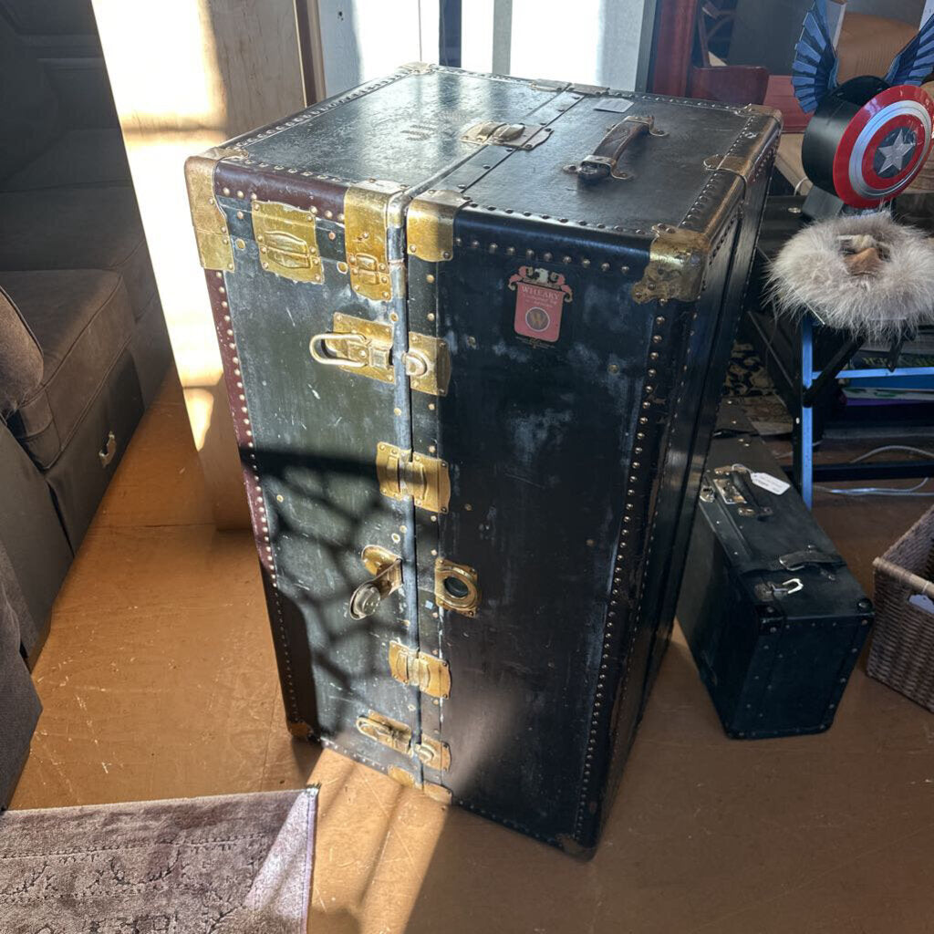 Vintage-style black trunk with gold accents on a wooden floor.