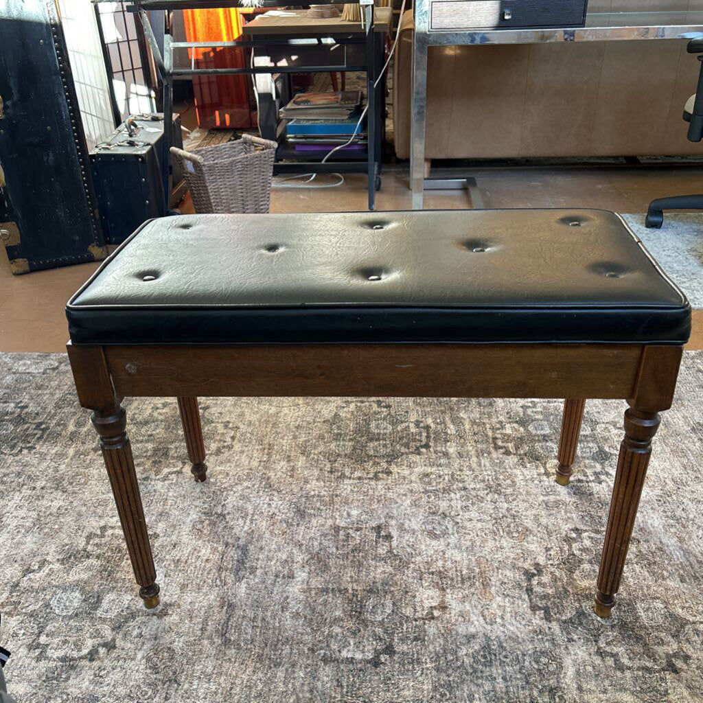 Dark brown wooden bench with black leather cushion on a textured gray floor.