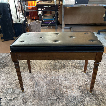 Dark brown wooden bench with black leather cushion on a textured gray floor.