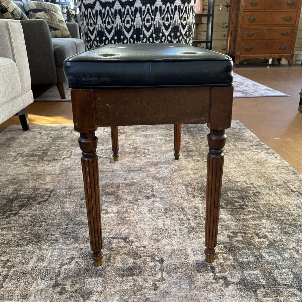 Wooden stool with a black cushion on a patterned rug in a room setting.