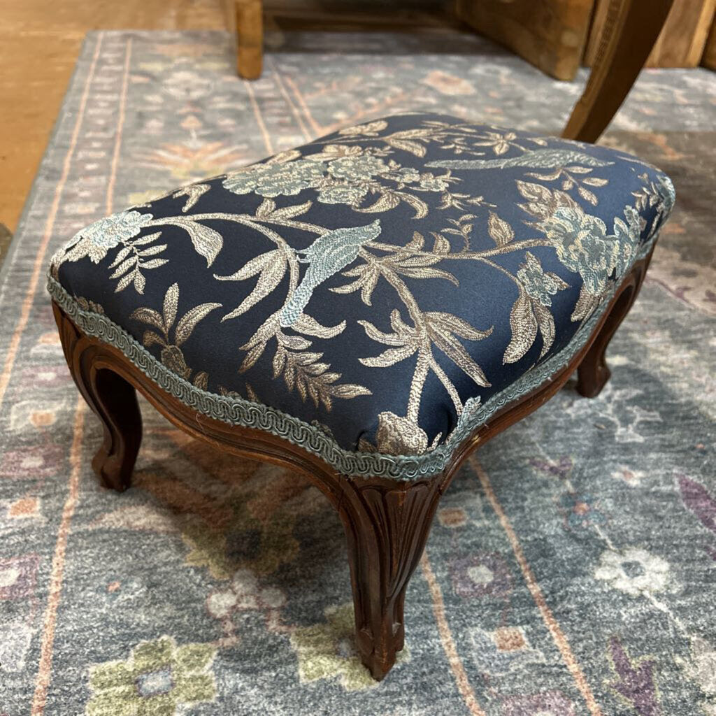 Small wooden stool with floral patterned cushion on a textured rug