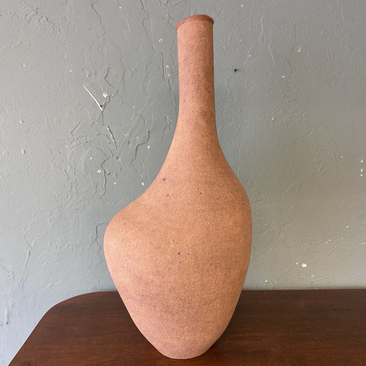 Terracotta-colored vase on a wooden surface with a light gray textured wall background