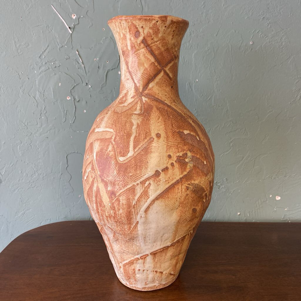 Ceramic vase with textured design on a wooden surface against a gray wall