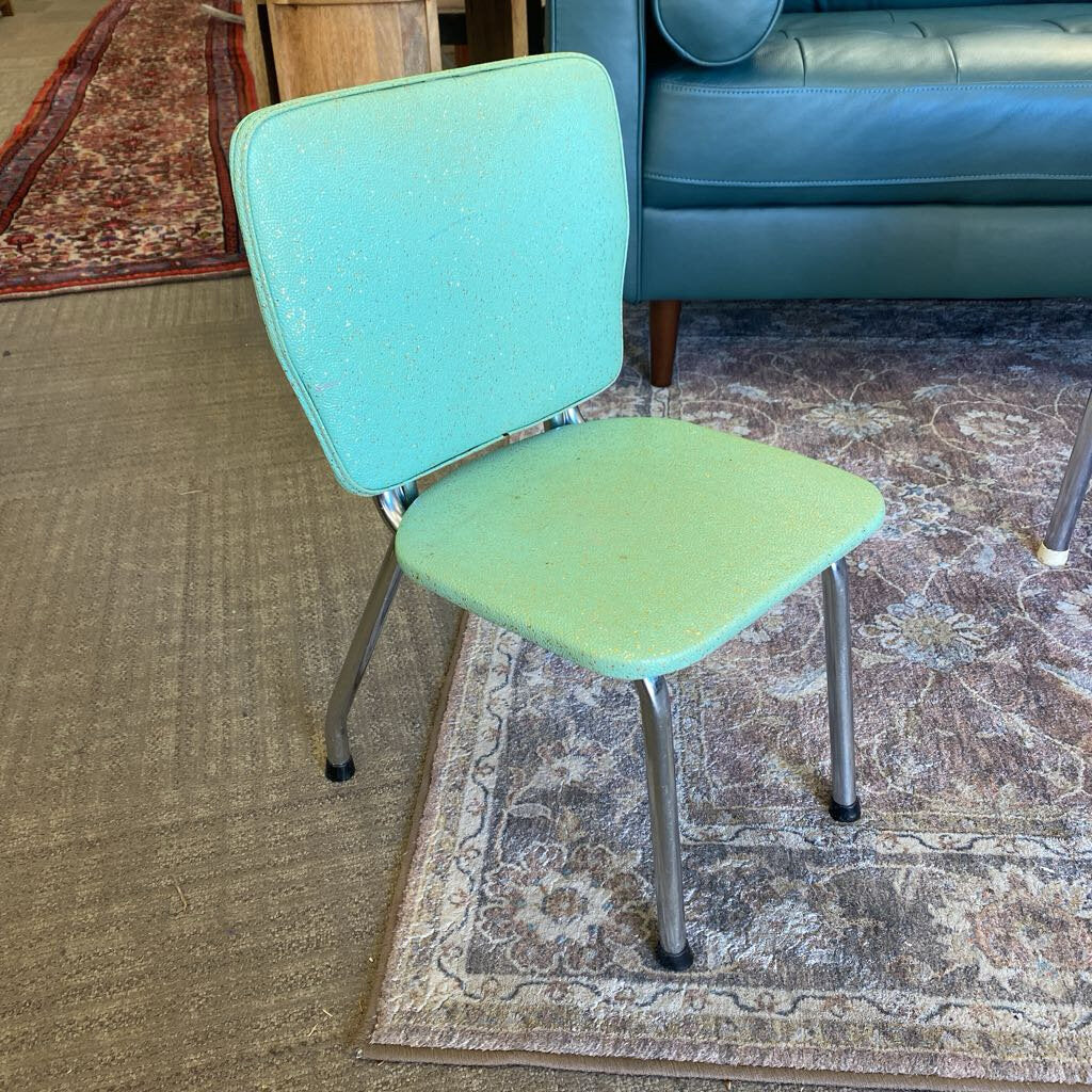 Green chair on a patterned rug with a blue couch in the background