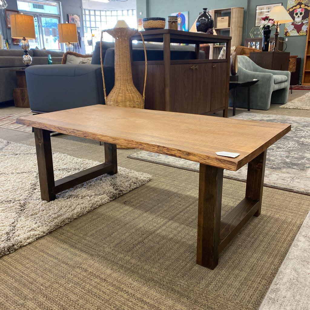 Wooden coffee table in a showroom setting with furniture and decor in the background.
