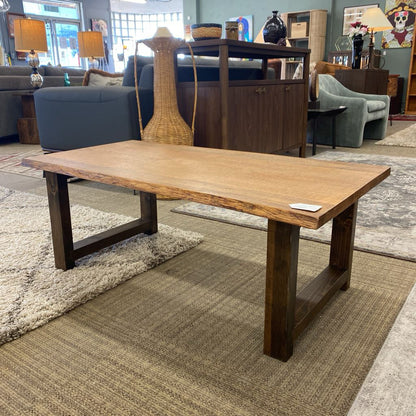 Wooden coffee table in a showroom setting with furniture and decor in the background.