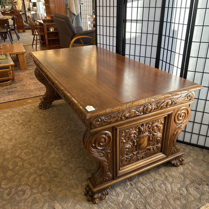 Carved wooden desk in a room with chairs and a rug.