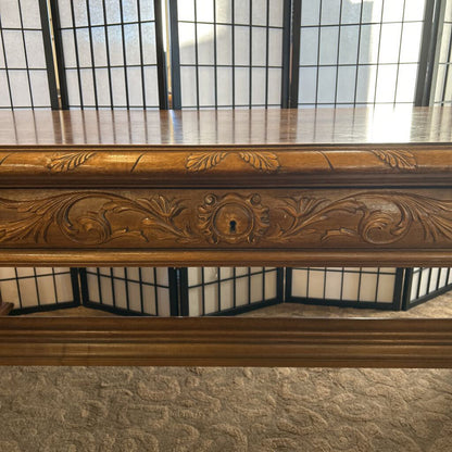 Decorative wooden mantel with intricate carvings in front of a large window.
