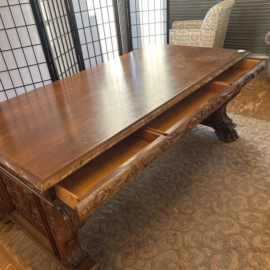 Wooden desk with intricate carvings in a room with a window and chair.