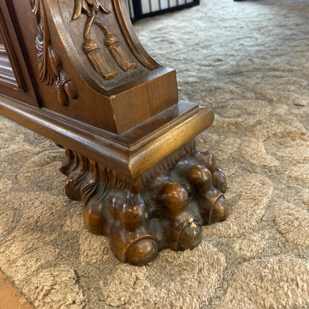 Carved wooden pedestal with intricate designs on a carpeted floor