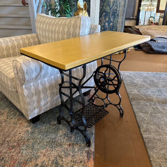 Wooden table with black metal base in a room with patterned carpet and furniture.