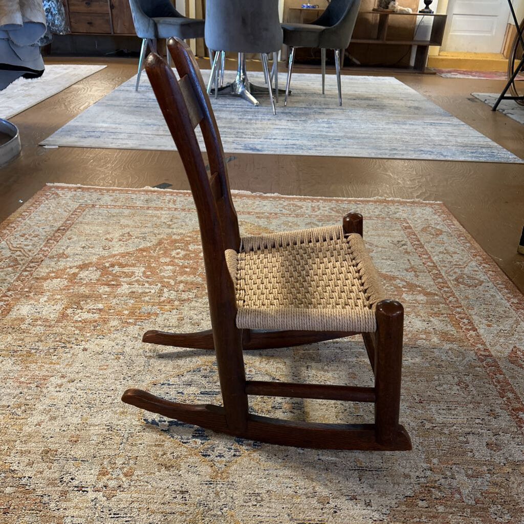 Wooden rocking chair with woven seat on a patterned rug in a room.