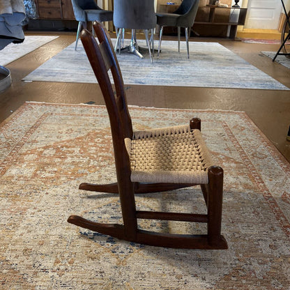 Wooden rocking chair with woven seat on a patterned rug in a room.
