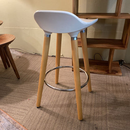 White bar stool with wooden legs on a textured floor.
