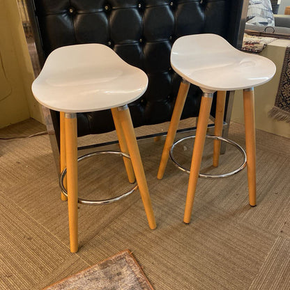 Two white bar stools with wooden legs on a carpeted floor.