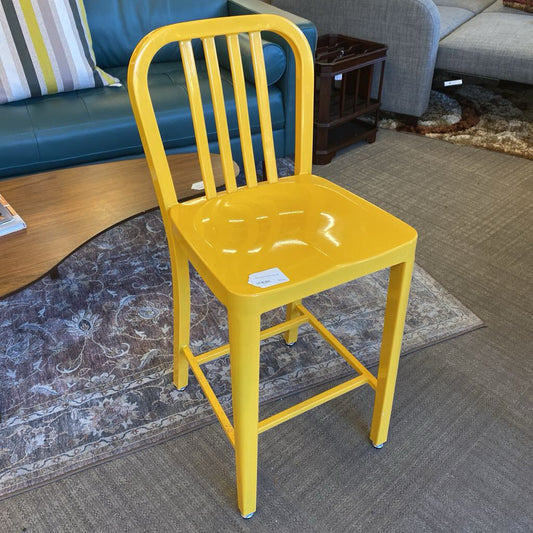 Yellow metal chair in a living room setting with a blue couch and wooden coffee table.
