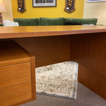 Wooden desk with green cushioned chairs against a yellow wall.