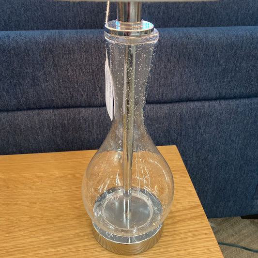 Clear glass bottle with silver base on a wooden surface against a blue upholstered background