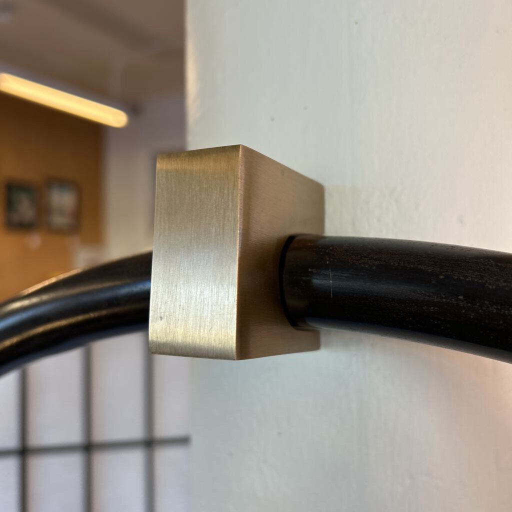 Close-up of a gold bracket attached to a black pipe against a neutral wall.
