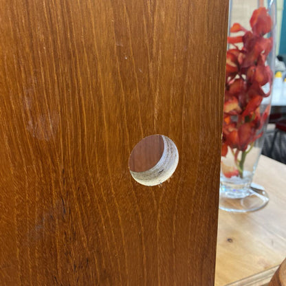 Wooden surface with a circular hole, possibly a door or furniture piece, with a glass vase of flowers in the background.