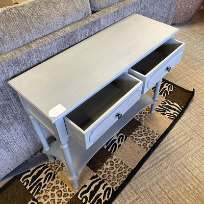 Small gray side table with two drawers in a living room setting.
