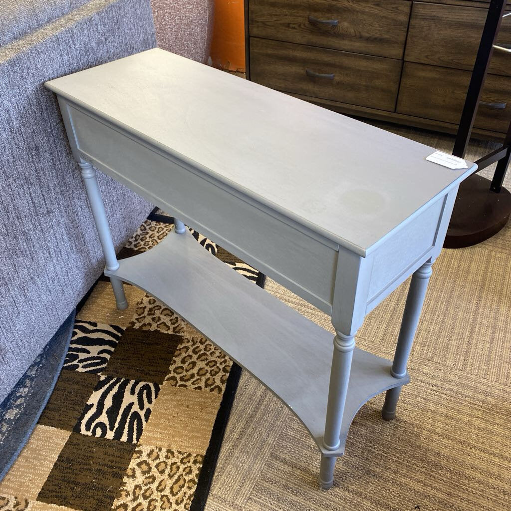 Light gray console table with a drawer and shelf in a room setting.