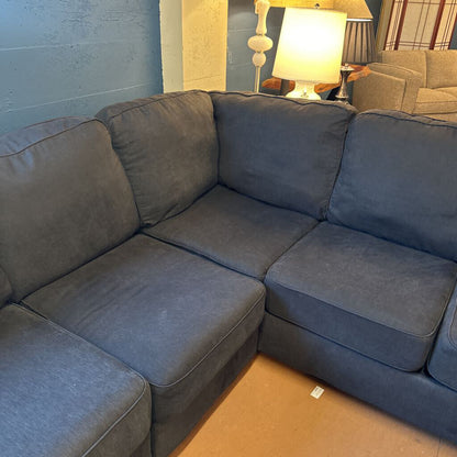 Gray sectional sofa in a living room setting with lamps and a wall.